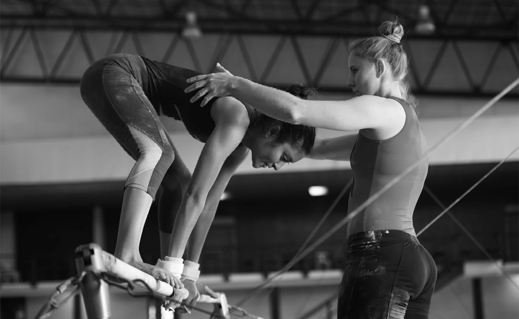 one woman helping another woman balance on a balance beam