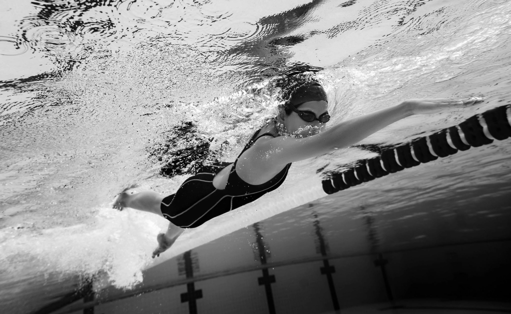 black and white underwater view of female swimmer in pool wearing swim cap and googles